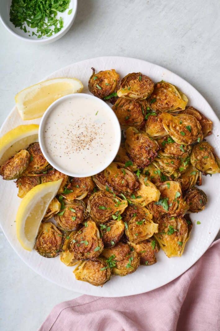 Smashed brussel sprouts on a plate with ranch sauce for dipping.