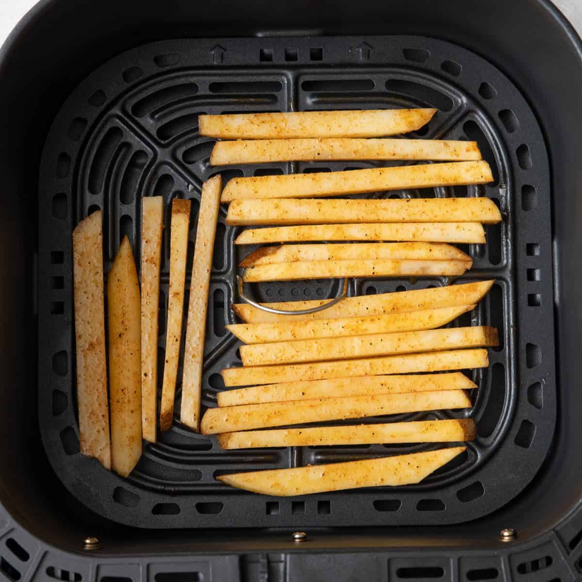 Seasoned fries in air fryer basket before cooking.