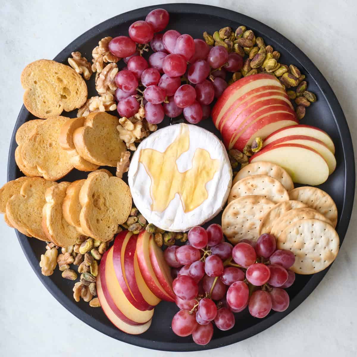 Appetizer platter with cheese in the center and fruits, nuts, and bread slices around.