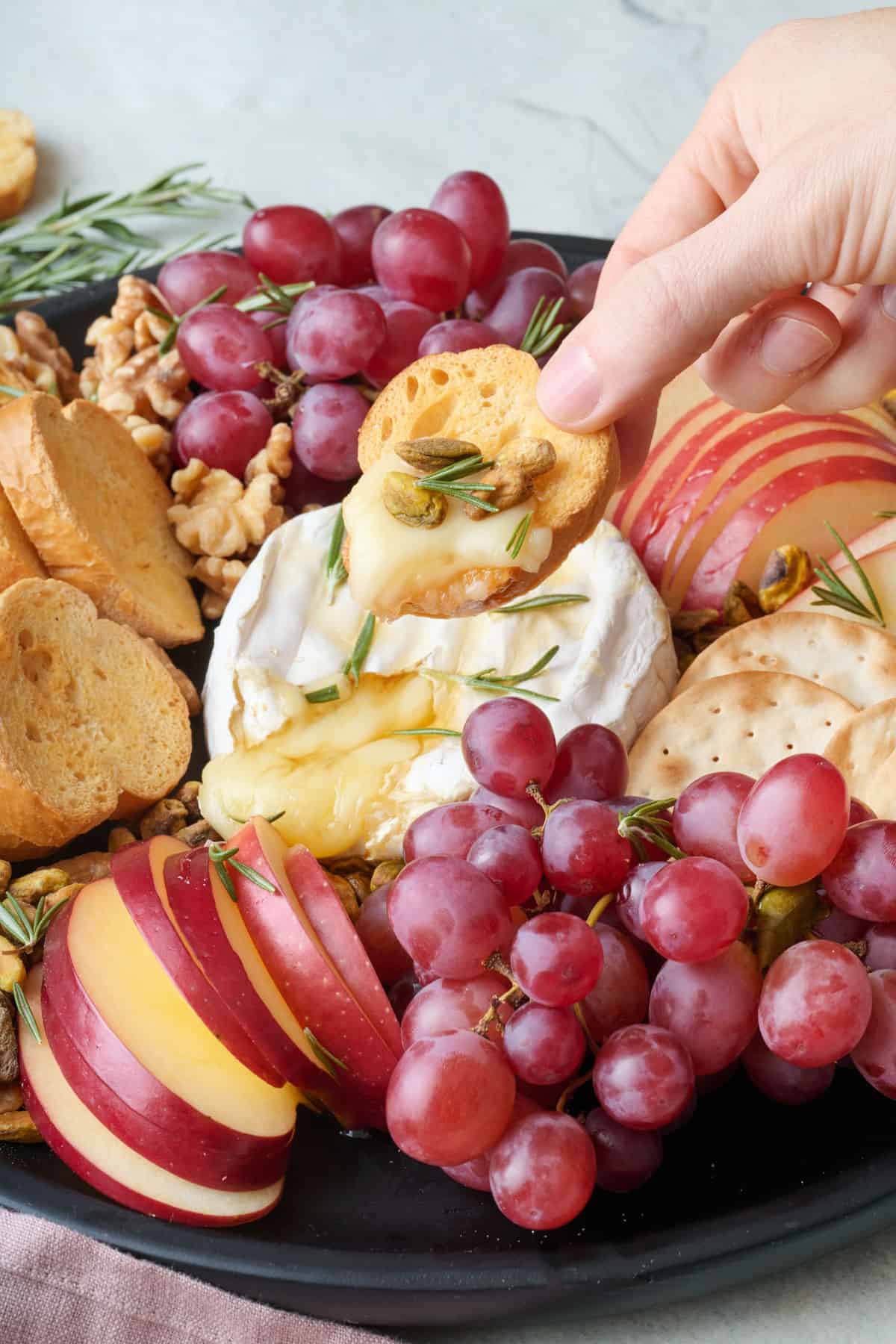 Toasted bread slice with brie and pistachios next to baked brie appetizer platter.