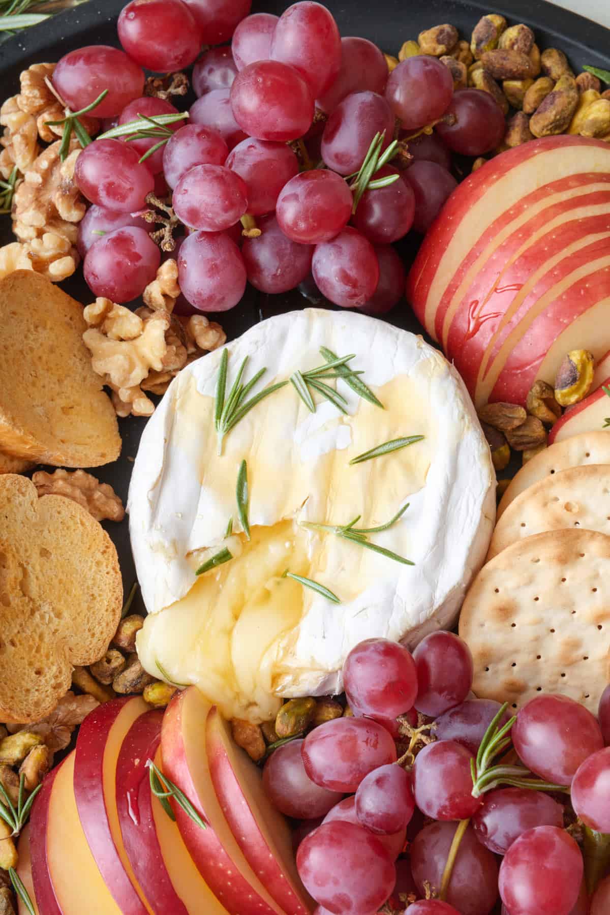 Close up of bake brie with cheese oozing out on a platter with fruit, crackers, and nuts.