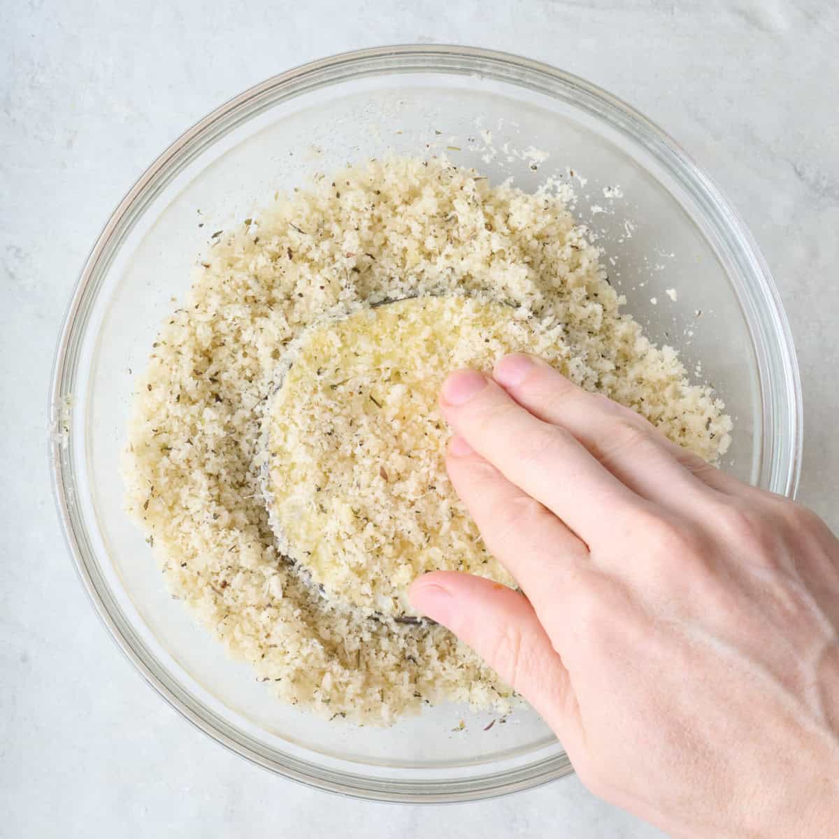 Pressing eggplant firmly into breadcrumbs.