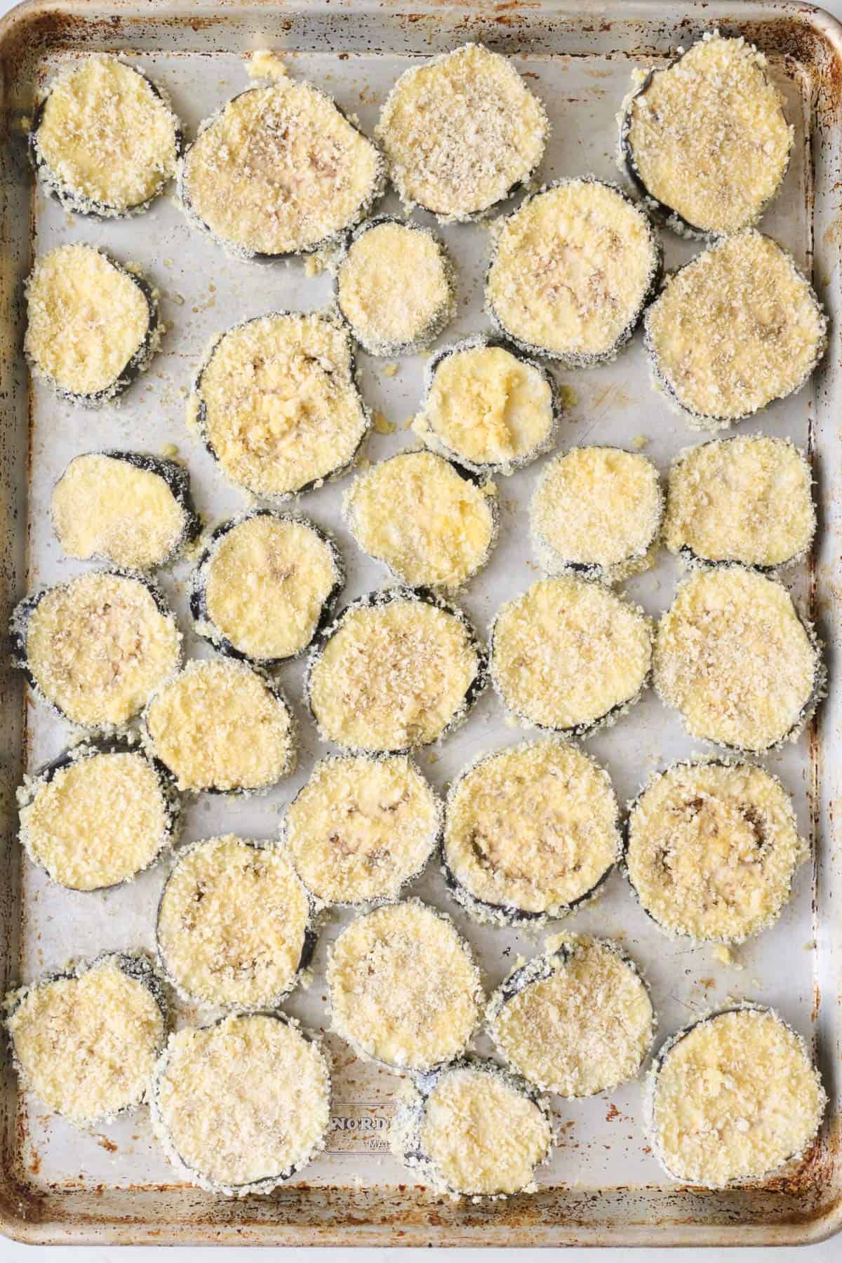 Breadcrumb coated eggplant slices on a baking sheet before baking.