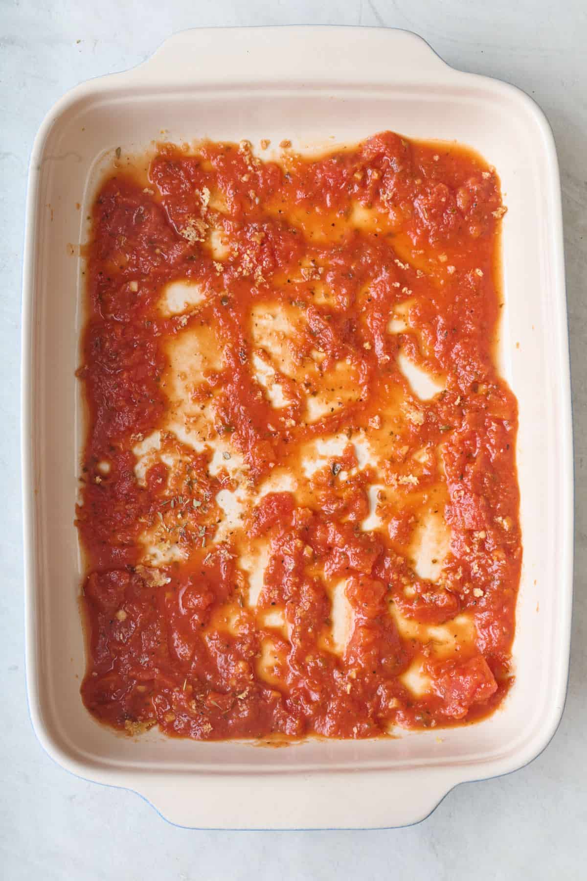 Marinara sauce spread evenly in the bottom of a baking dish.