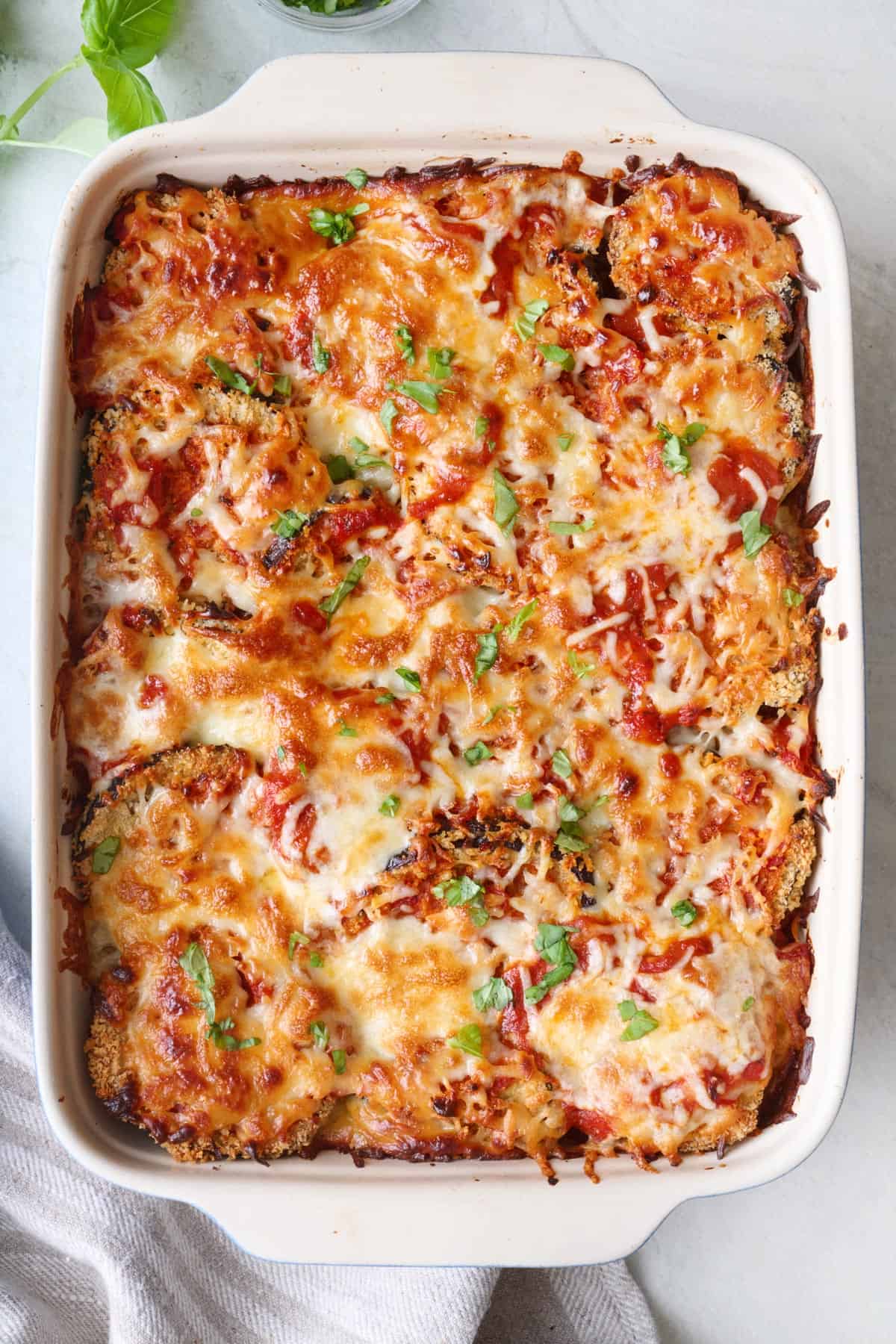 Baked eggplant parmesan in a baking dish garnished with fresh basil.