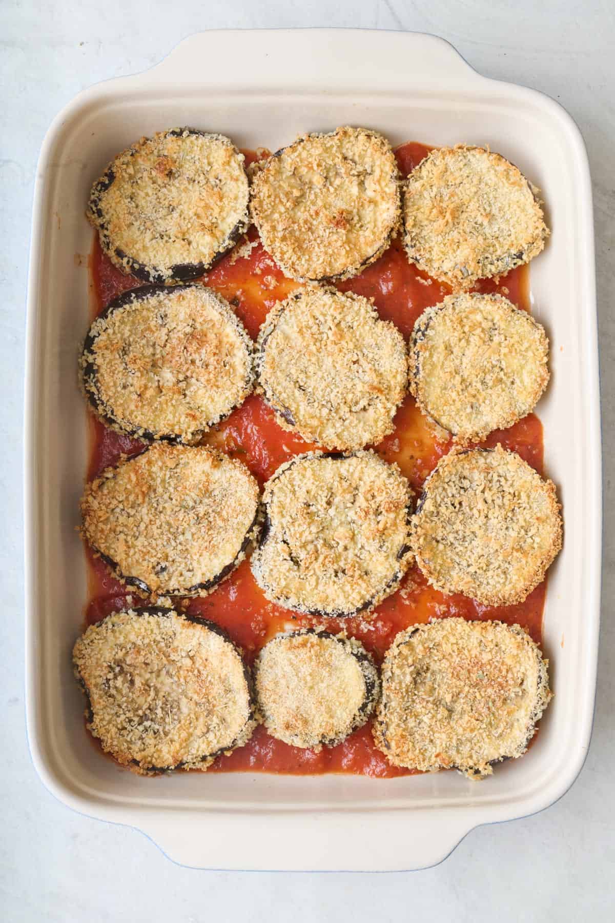 Breadcrumb coated eggplant slices on top of marinara sauce in a baking dish.