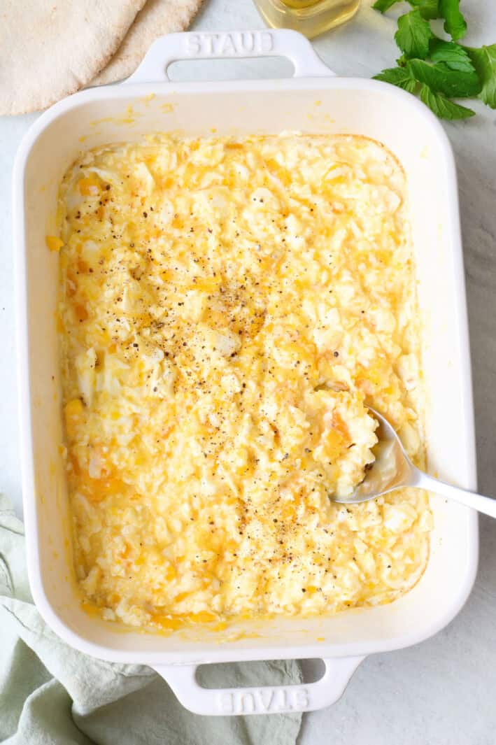 Baked scrambled feta eggs in a baking dish with a spoon dipped in.