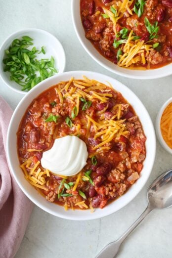 Two bowls of ground beef chili topped with greek yogurt and shredded cheese.