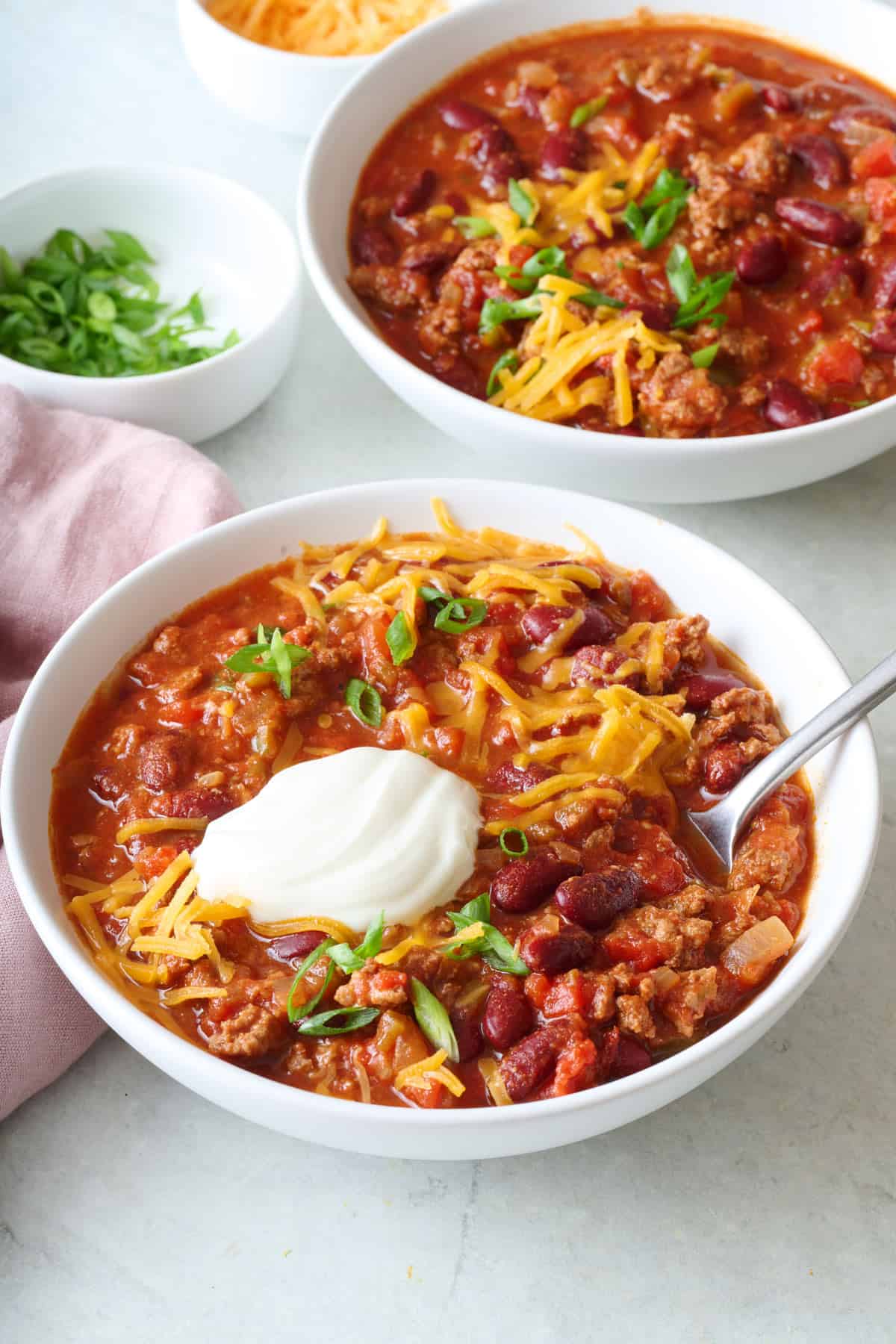 Two bowls of beef chili with toppings.