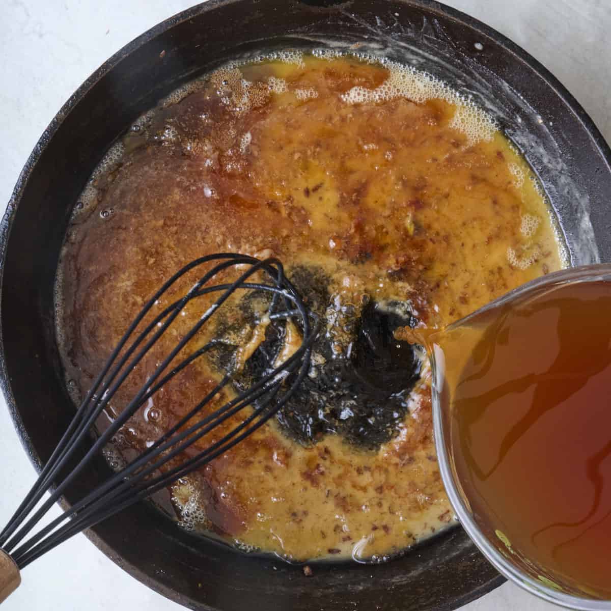 Beef broth and seasonings being poured into roux.