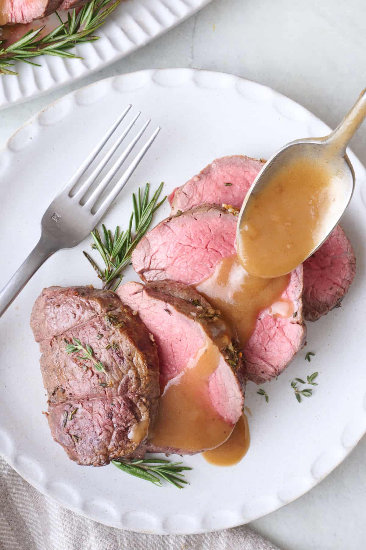 Spooning gravy over sliced beef tenderloin.