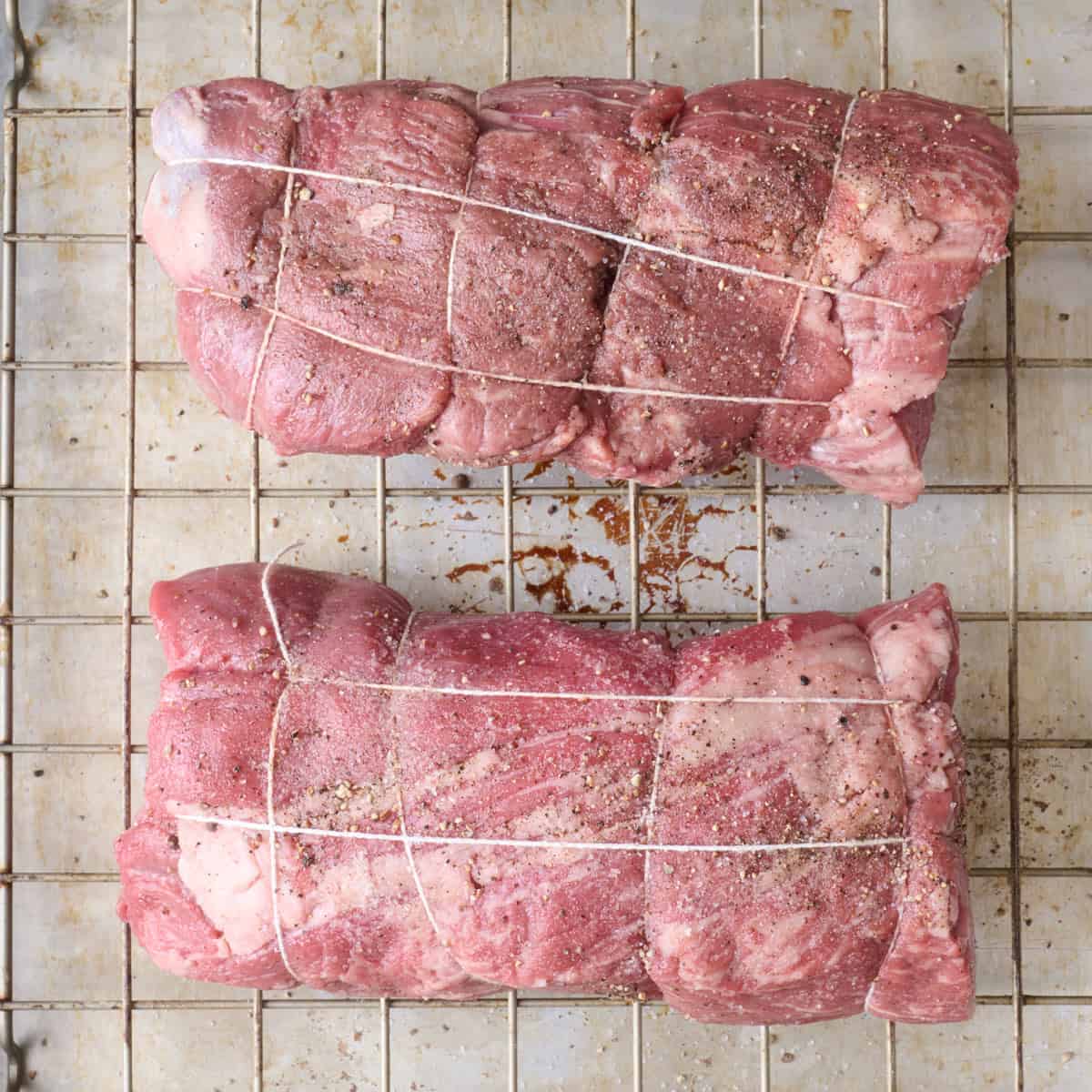 Two pieces of beef tenderloin wrapped in twin on a wire rack and seasoned.