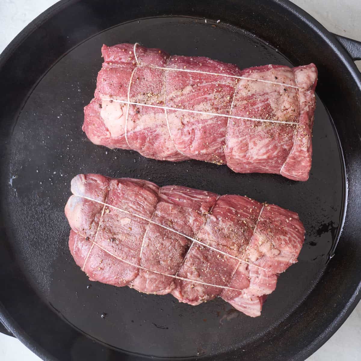 Twine wrapped and seasoned beef tenderloin pieces in an oiled cast iron skillet.