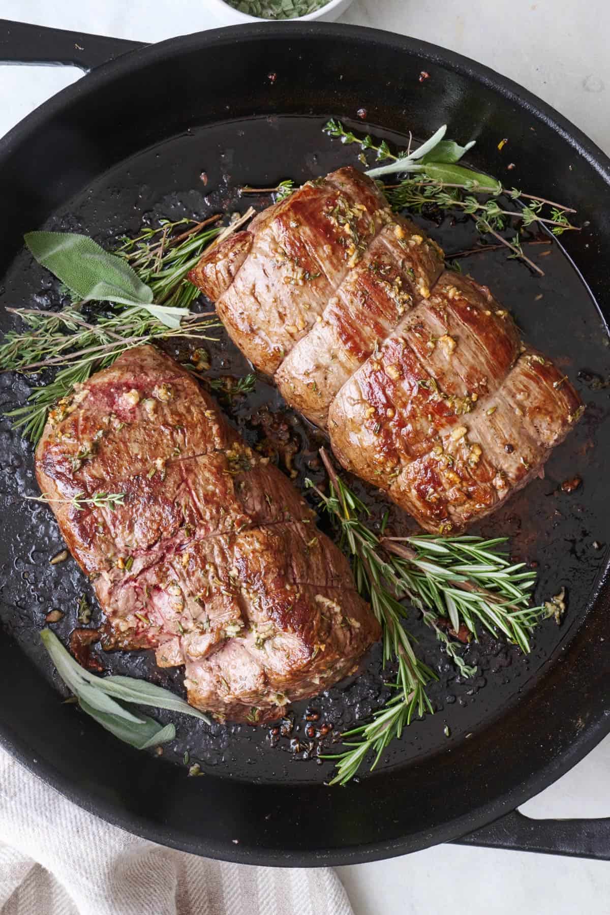 Beef tenderloin roast in a cast iron skillet with extra fresh herbs.