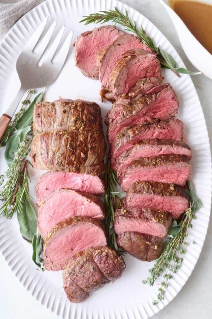 Beef tenderloin roast sliced into thick pieces and fanned out on a large oval platter.