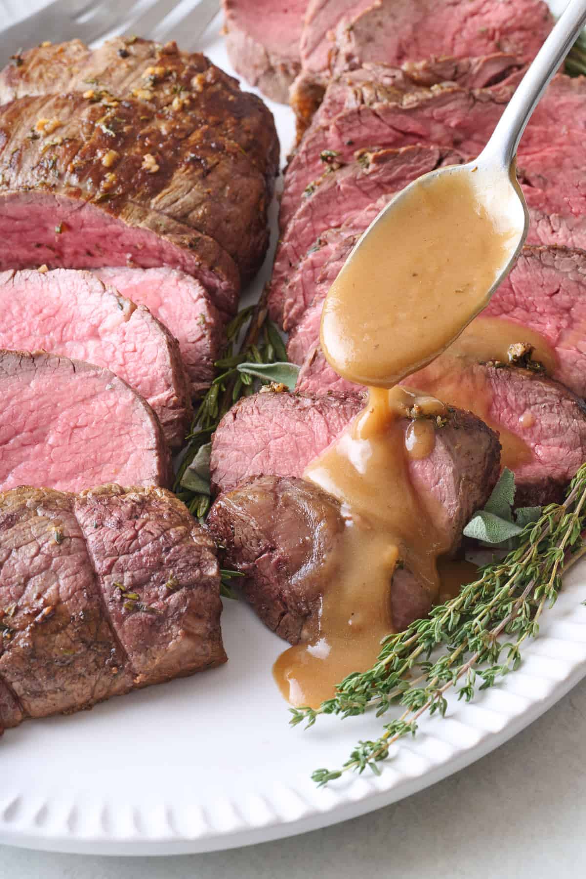 Spooning gravy over sliced beef tenderloin.