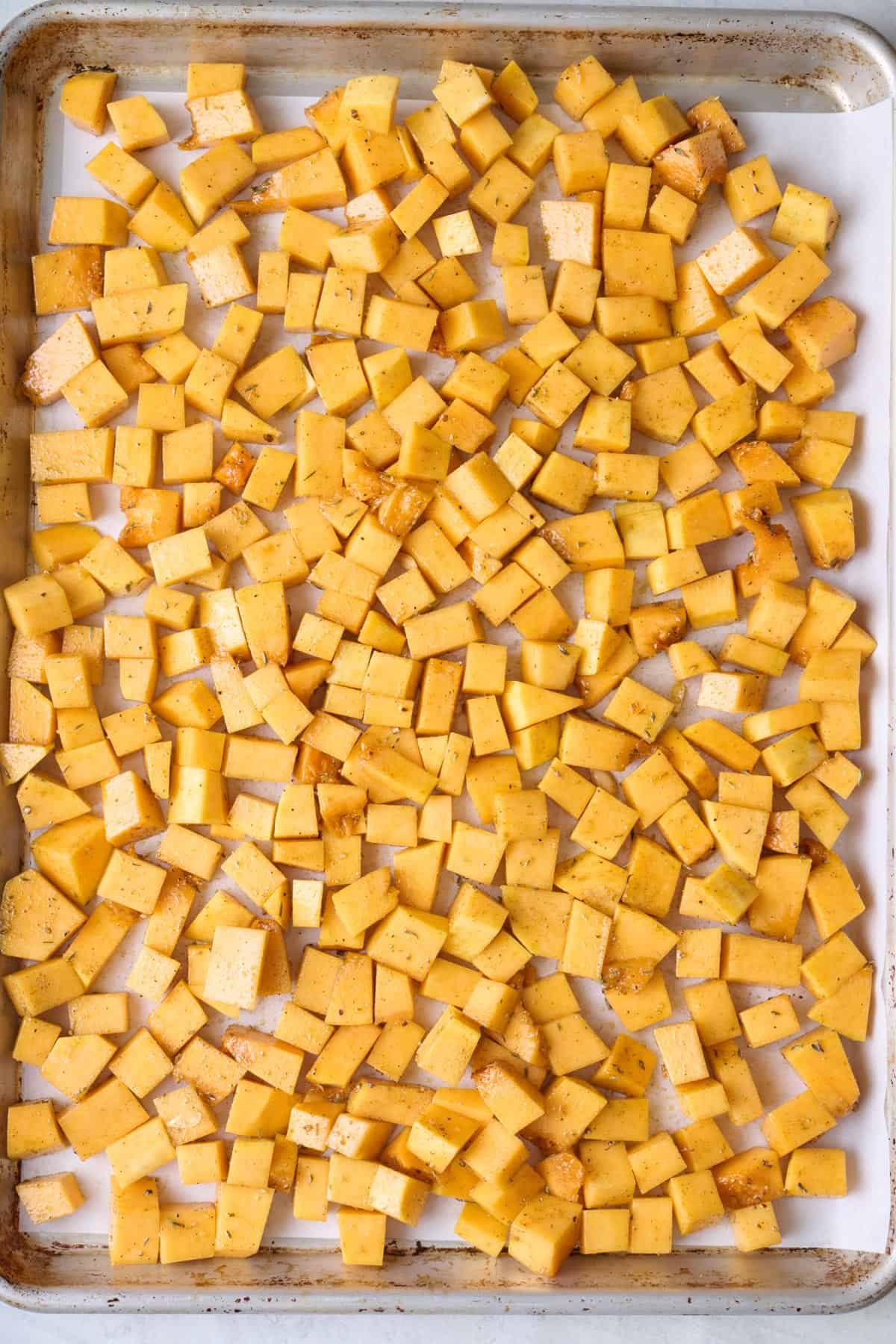 Butternut squash cubes coated in oil and spices on a baking sheet before roasting.