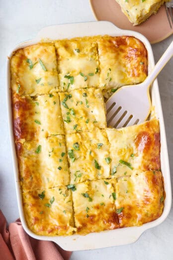 Butternut squash lasagna cut into 12 servings with one removed to a plate nearby and spatula dipped into dish.