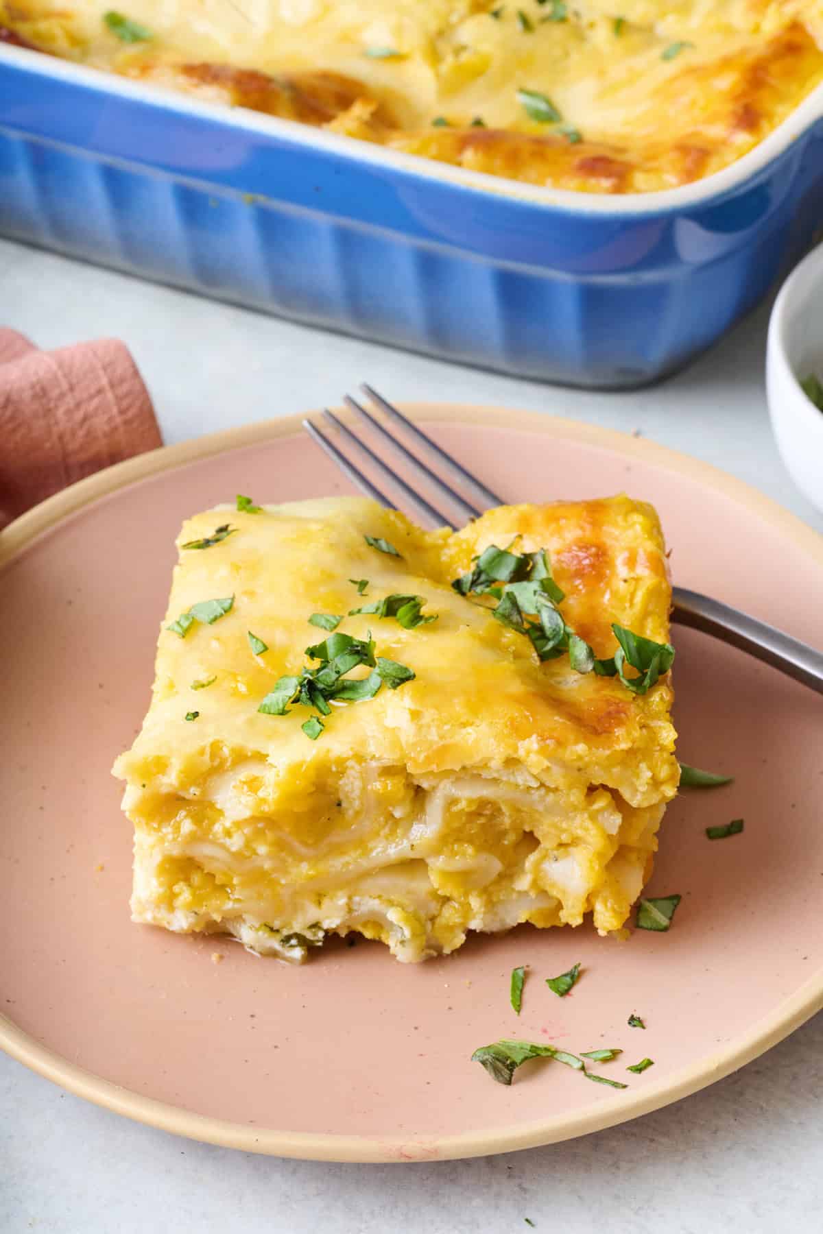 Serving of butternut squash lasagna on a plate with baking dish nearby.