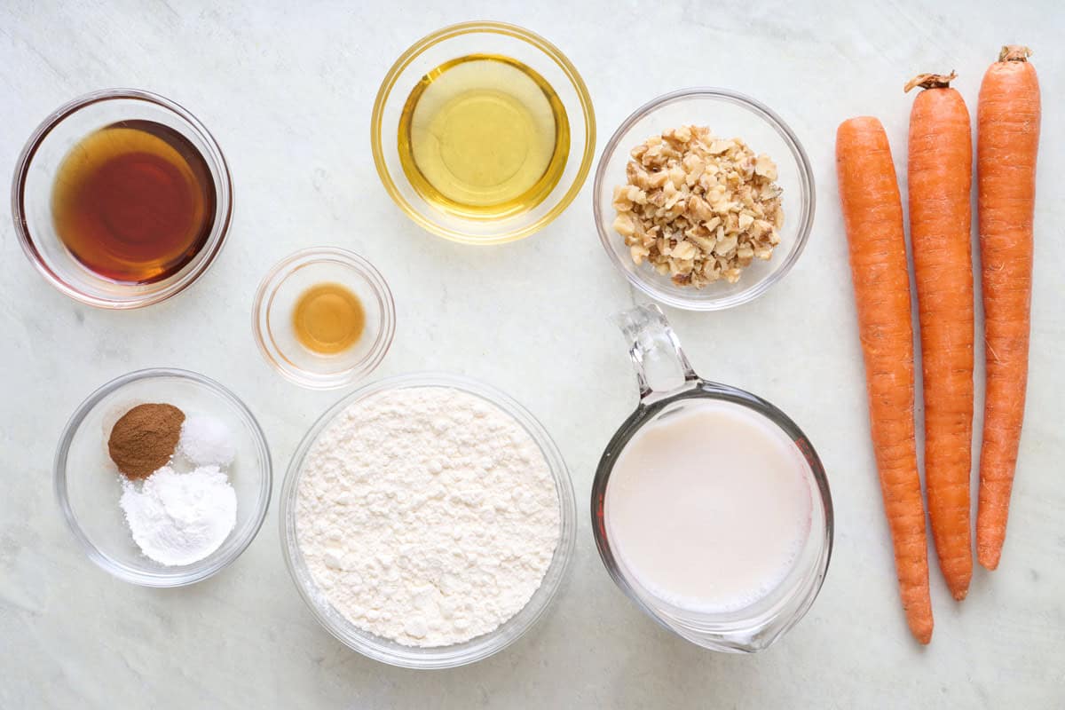 Ingredients for recipe before prepping: maple syrup, baking powder, salt and cinnamon, vanilla, oil, flour, milk, walnuts, and carrots.