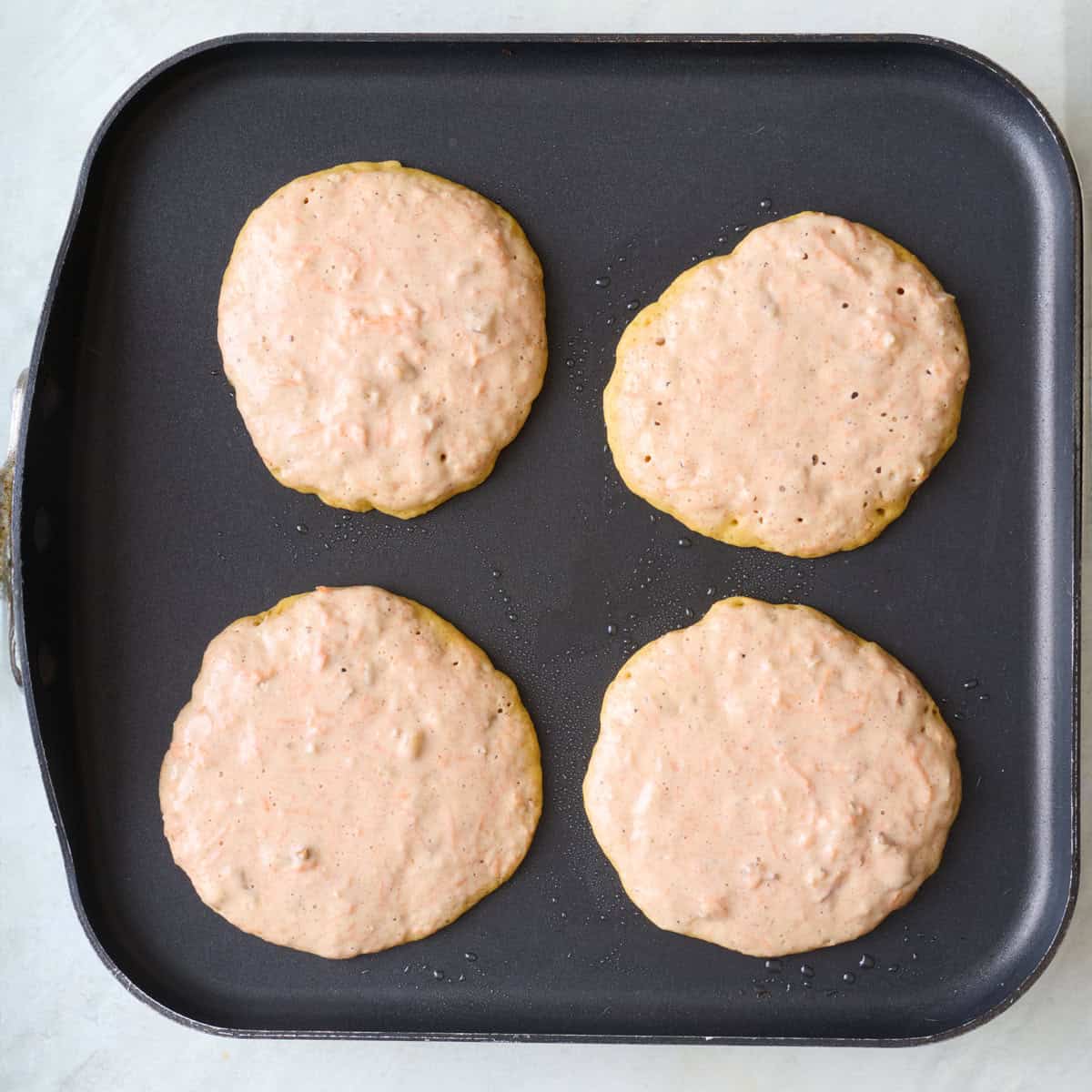 4 pancakes on a griddle with edges firming up.