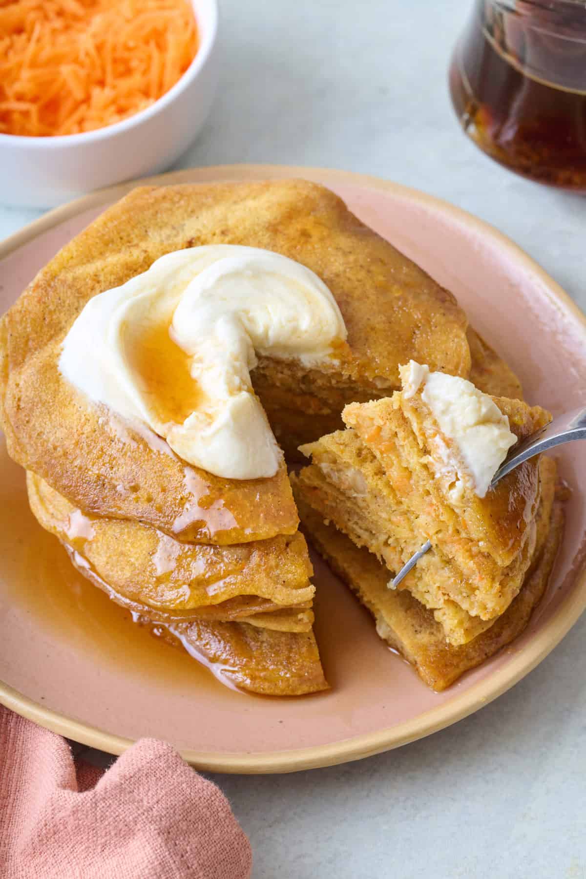 Fork pulling back a bite of carrot cake pancakes away from stack to show inside texture.