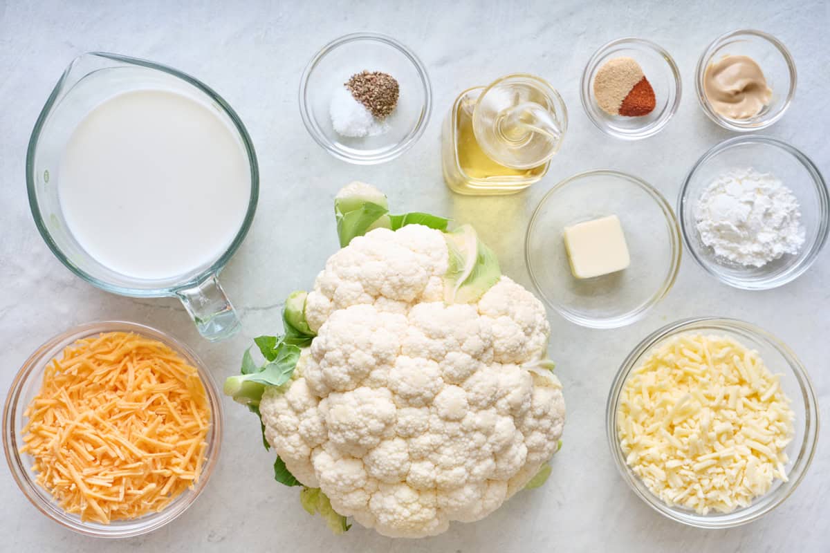 Ingredients for recipe before prepping: cauliflower, milk, shredded cheese, seasonings, oil, butter, Dijon mustard, and cornstarch.