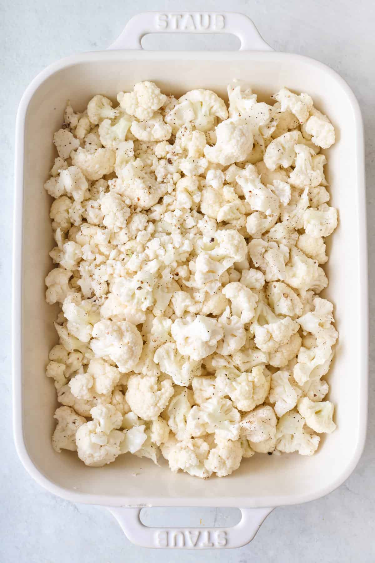 Cauliflower florets in baking dish coated with oil, salt and pepper.