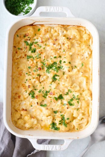 Baked cauliflower mac & cheese recipe in baking dish, garnished with fresh parsley.