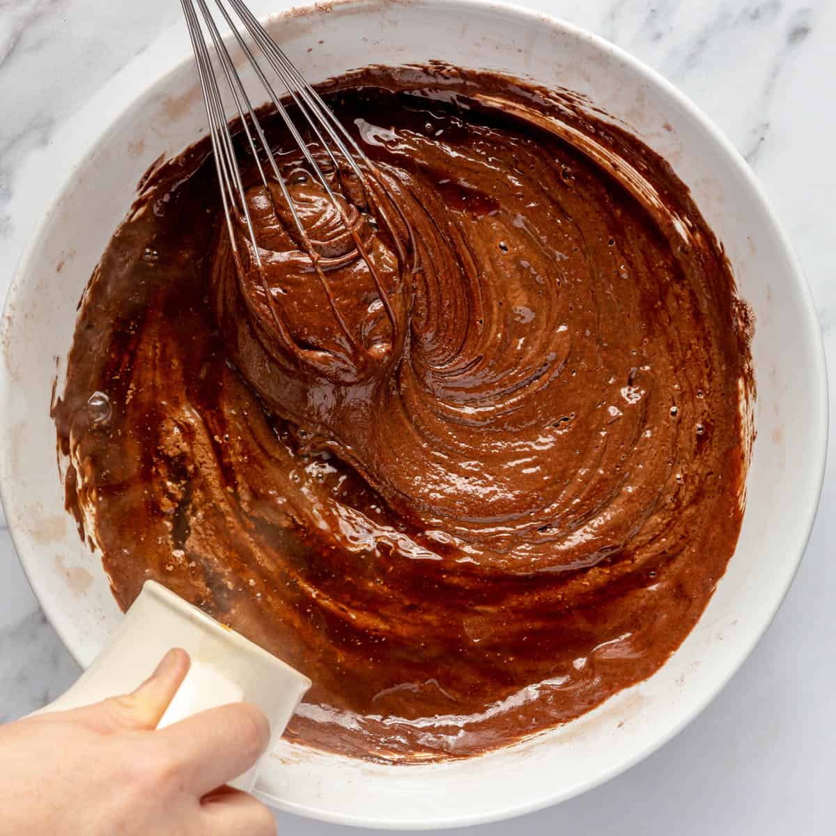 Pouring hot water into chocolate batter while stirring.