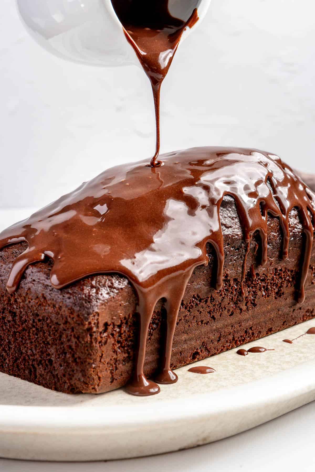 Pouring chocolate glaze over chocolate loaf cake.