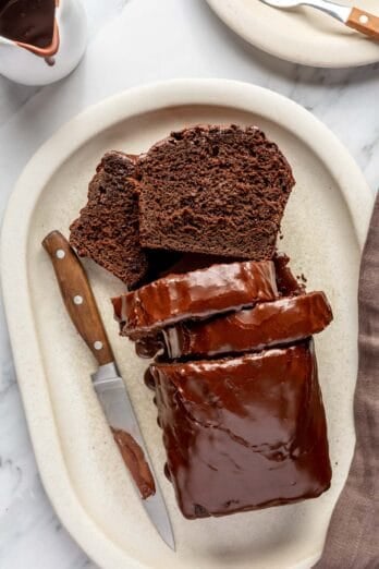 Chocolate loaf cake on a serving platter with chocolate glaze and a few slices cut.