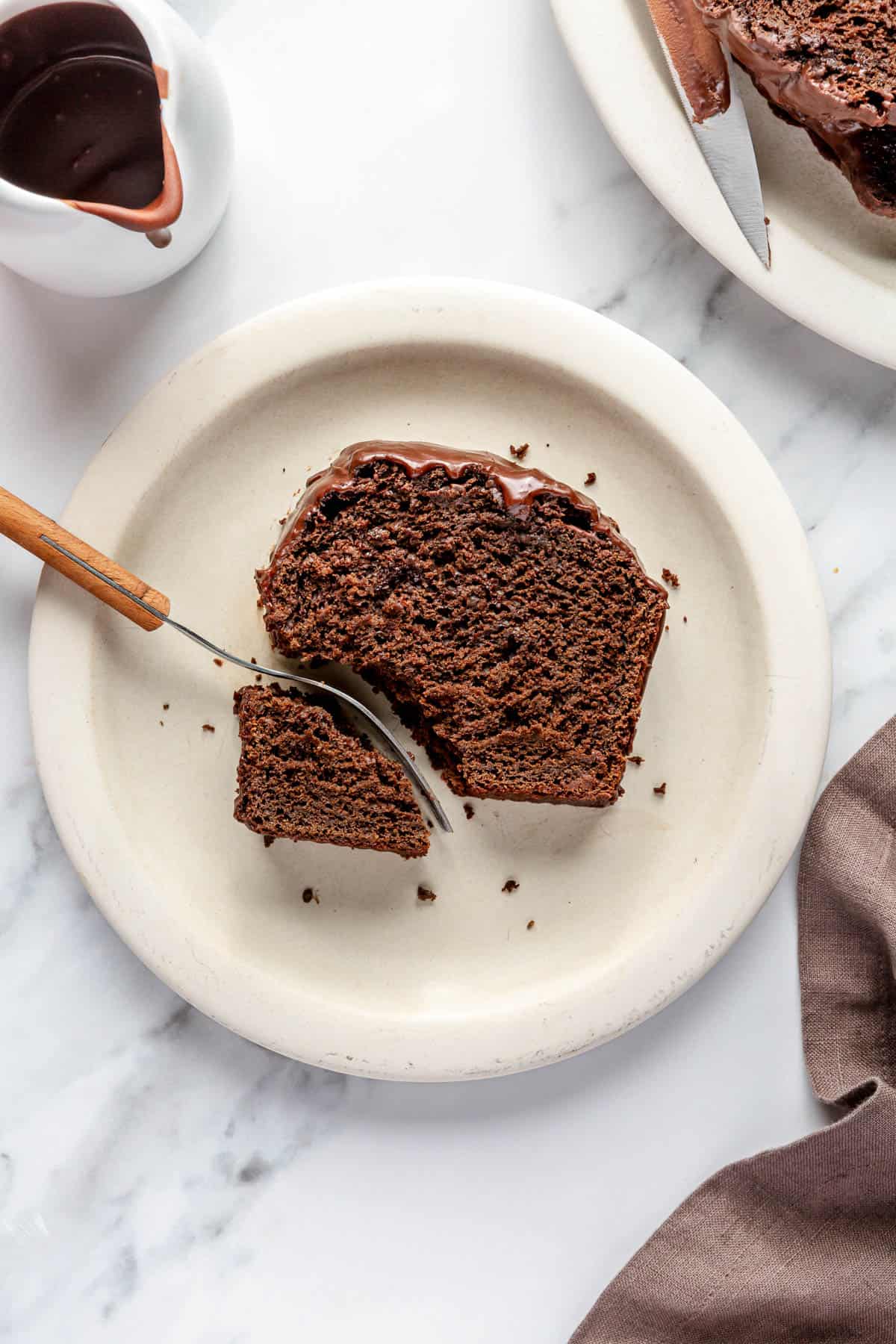 Slice of chocolate loaf cake on a small plate with a piece broke off with fork.