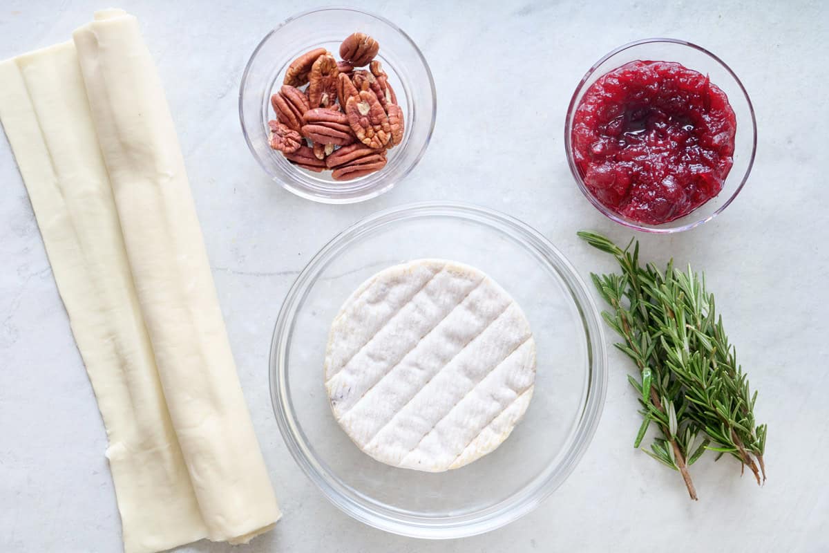 Ingredients for recipe: puff pastry, pecans, brie wheel, cranberry sauce, and fresh rosemary.