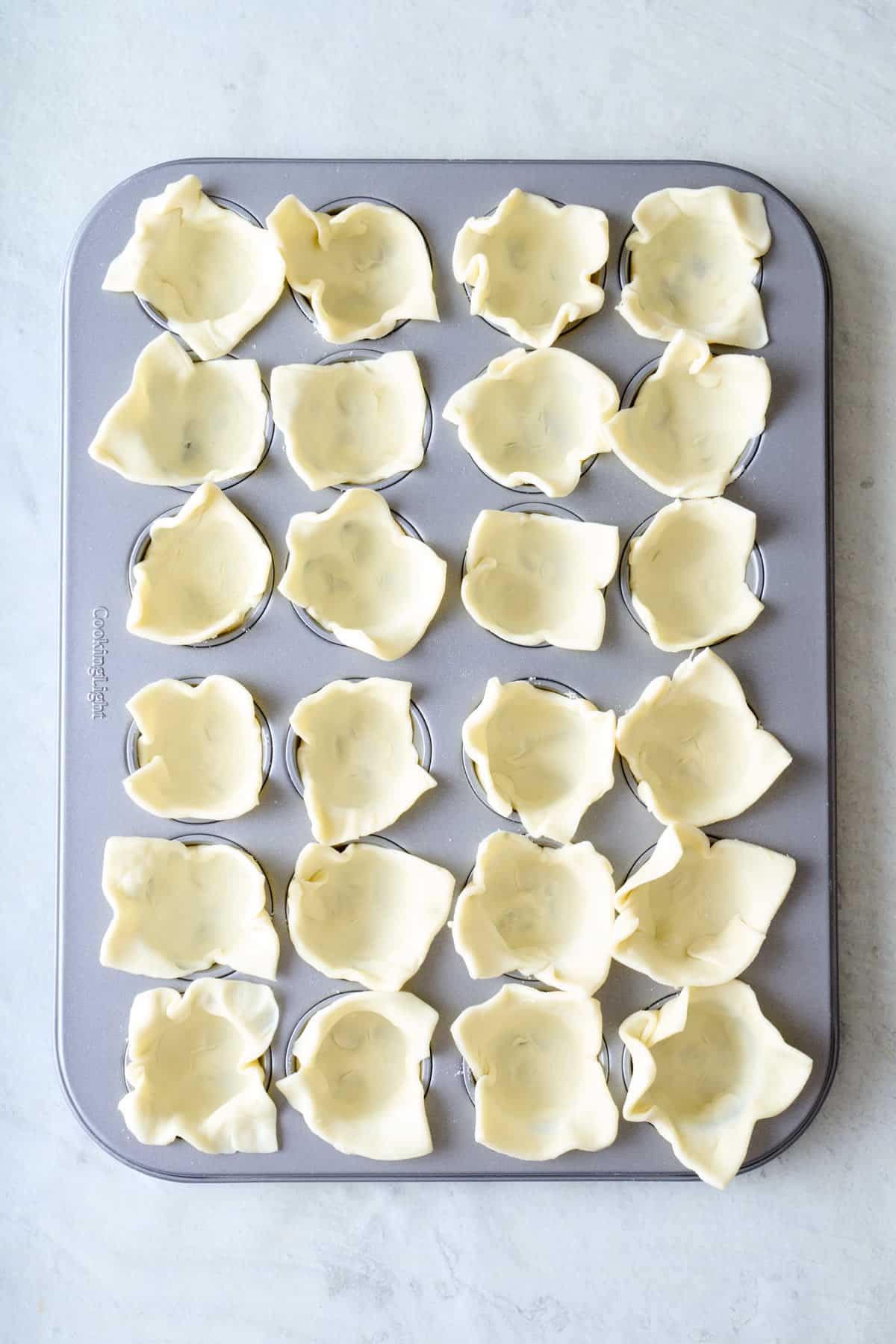 Mini muffin pan with puff pastry squares pressed into each cup.