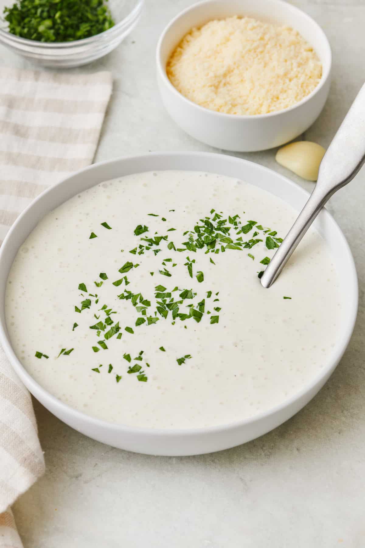 Homemade healthy alfredo sauce in a bowl with a spoon dipped inside.