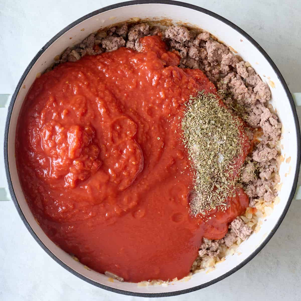 Crushed tomatoes and seasoning added to cooked crumbled ground beef.