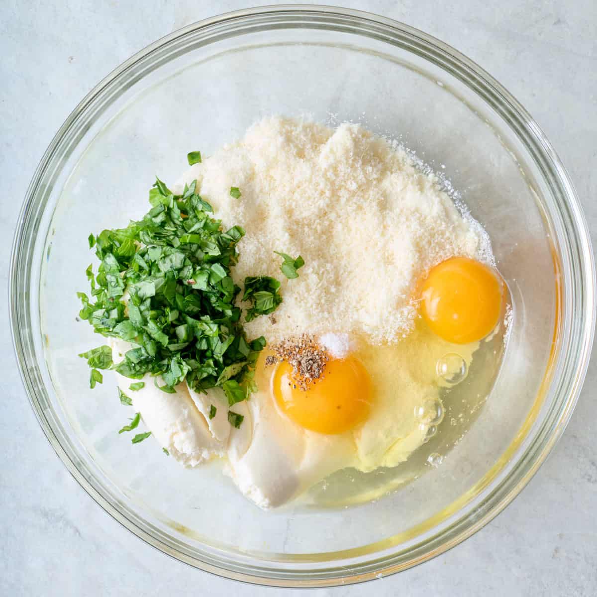 Ricotta, parm, basil, egg, salt and pepper in a bowl.