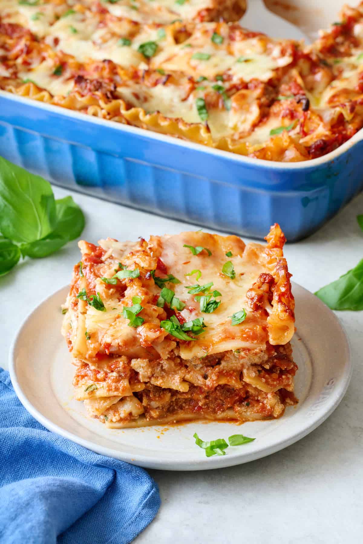 Slice of homemade lasagna on a small plate to show each layer with baking dish nearby.