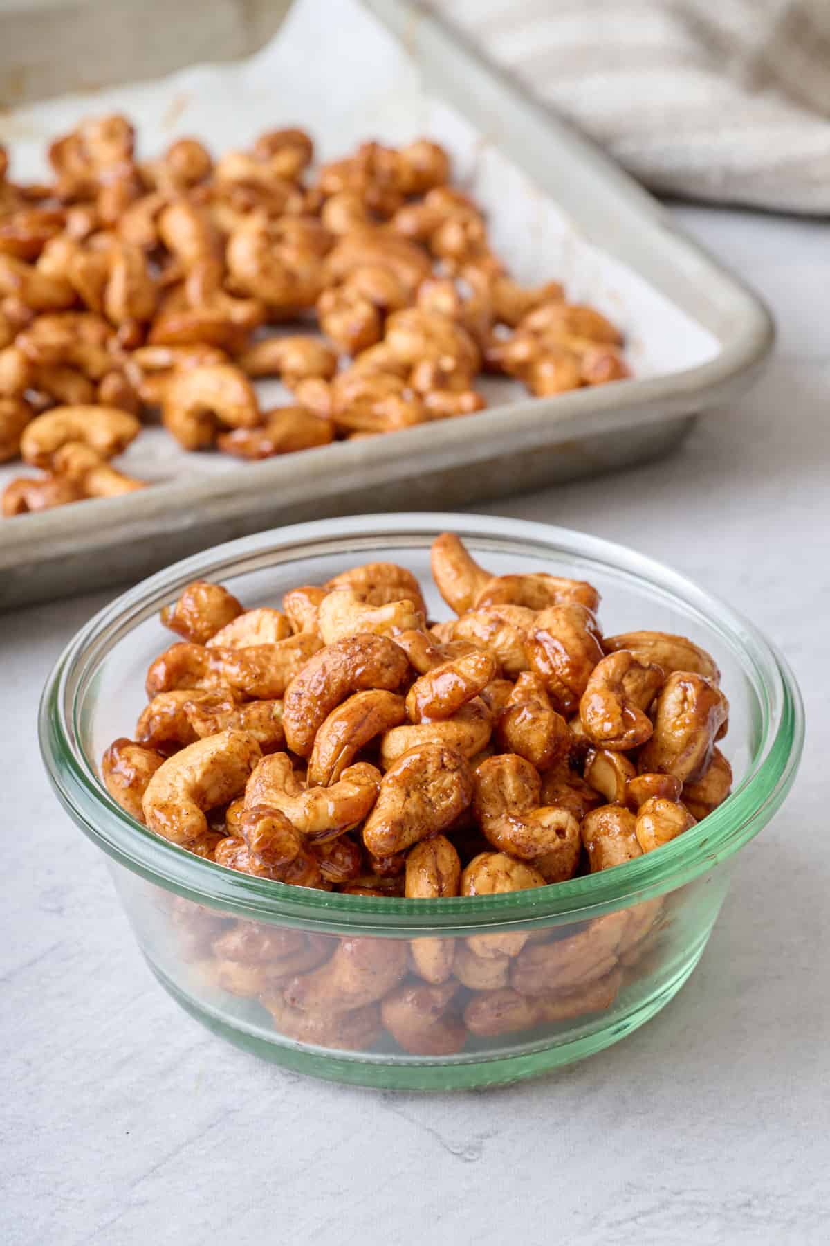 Small dish of honey roasted cashews with baking sheet of more nearby.