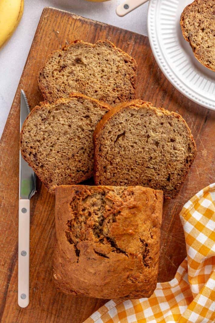 Banana bread on cutting board with a few slices cut and laying down, one slice on a plate nearby.