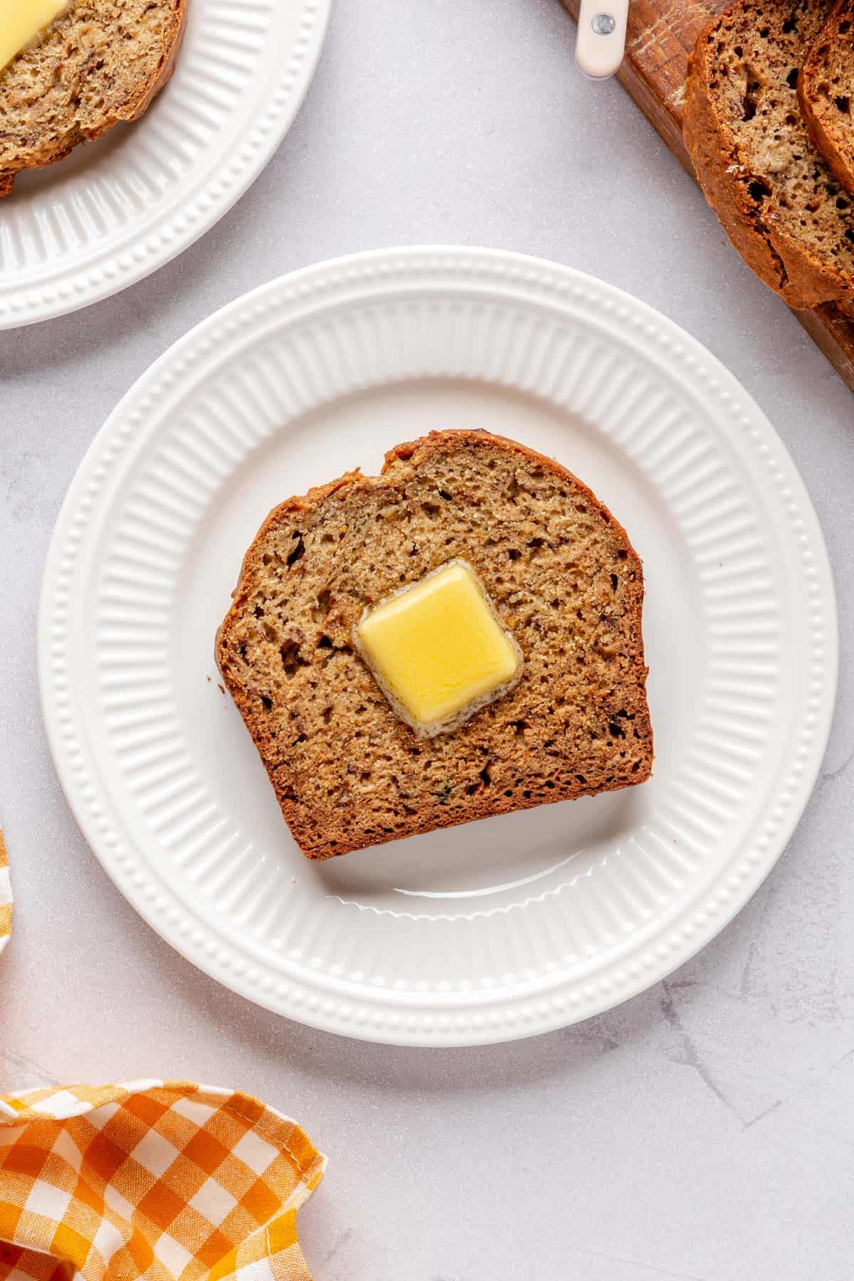 Slice of banana bread on a small plate with a pat of butter.