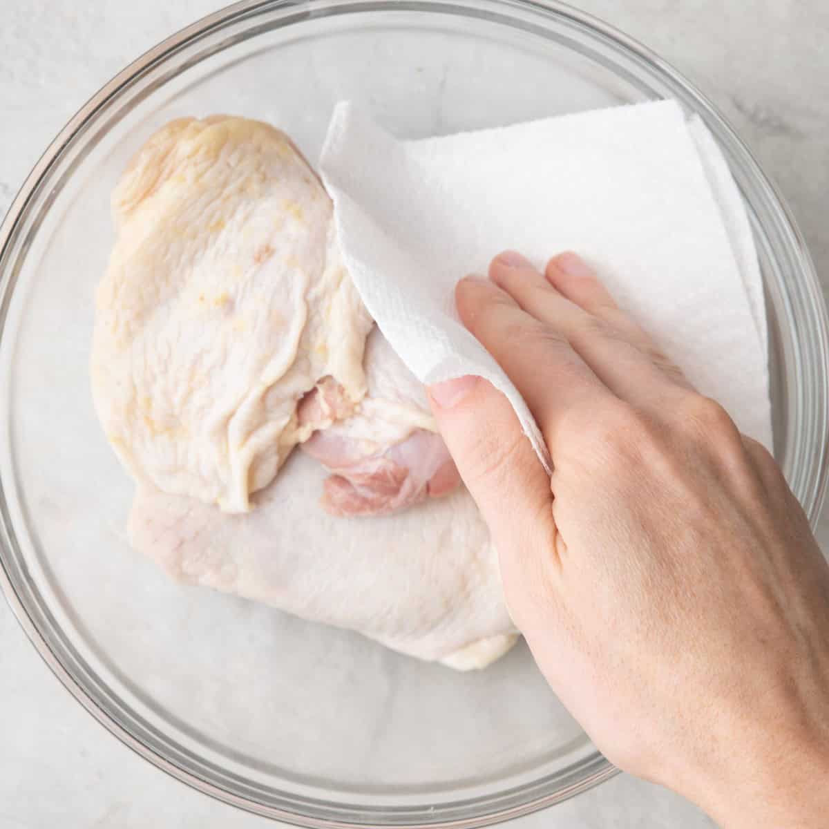 Chicken thighs in a bowl being patted dry with paper towels.