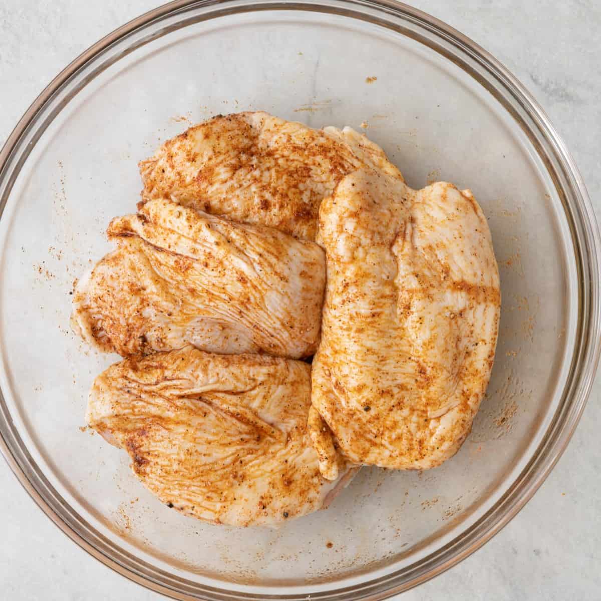 Chicken after being coated with seasoning in a bowl.