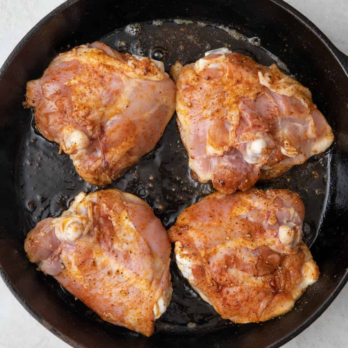 Seasoned chicken thighs skin side down on skillet.