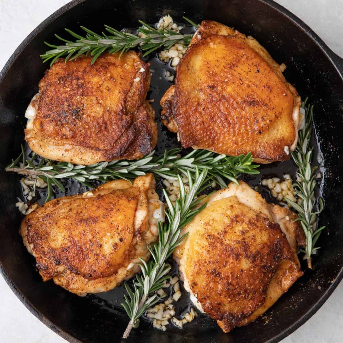 Rosemary sprigs and garlic added to cast iron skillet with chicken before baking.