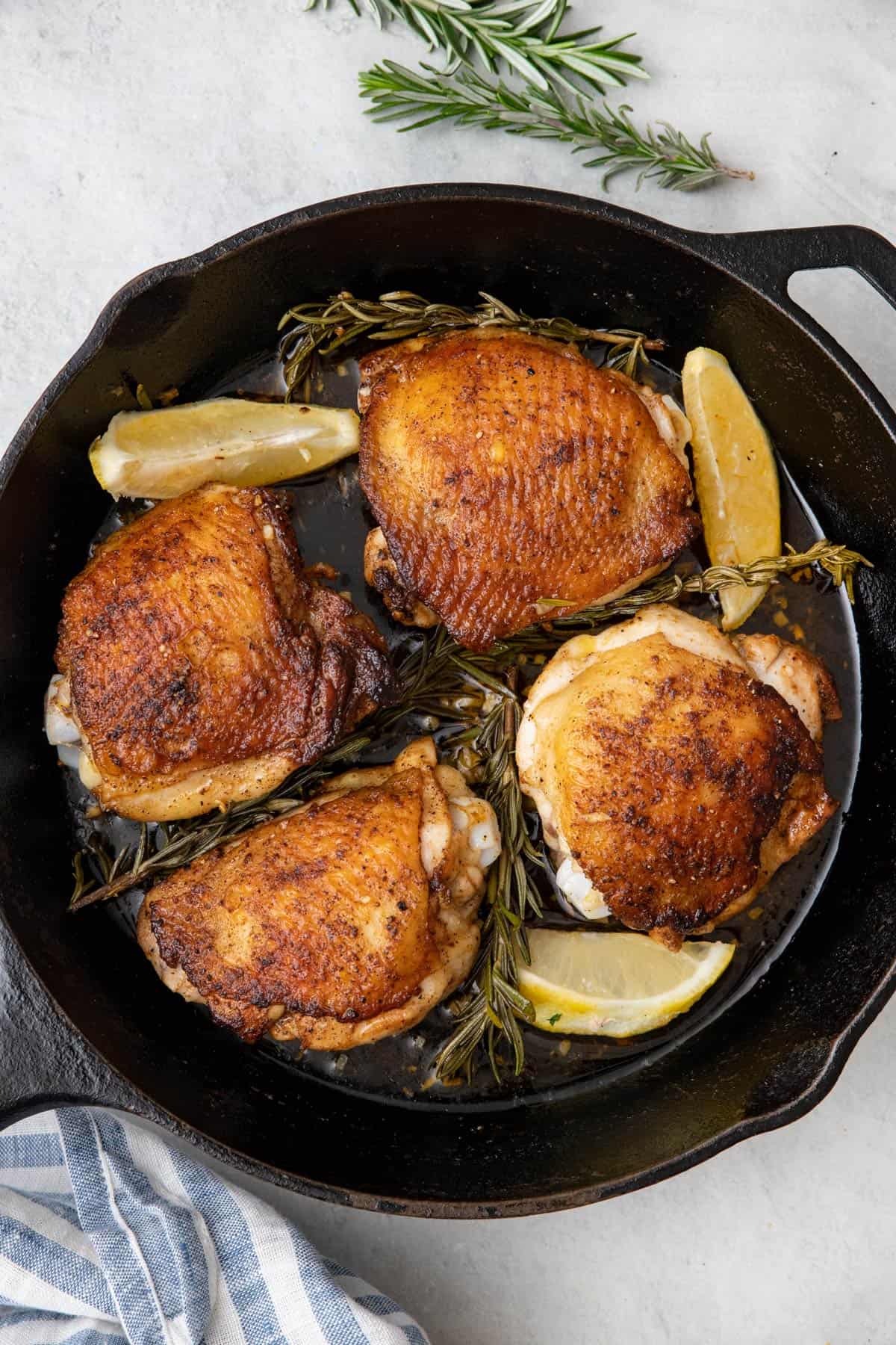 Skillet rosemary chicken thighs in cast iron pan after baking with crispy skin.