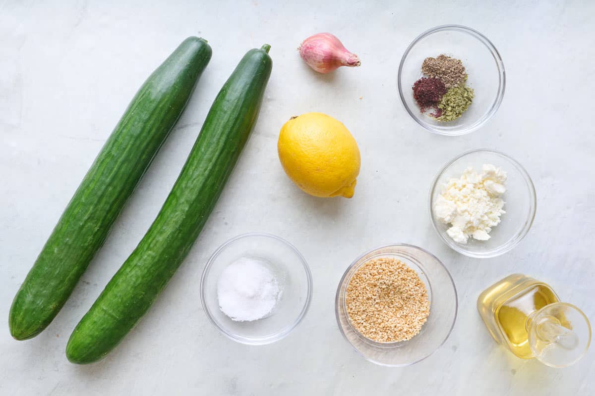 Ingredients for recipe: English cucumbers, lemon, shallot, salt, dried mint, sumac, black pepper, crumbled feta cheese, sesame seeds, and oil.