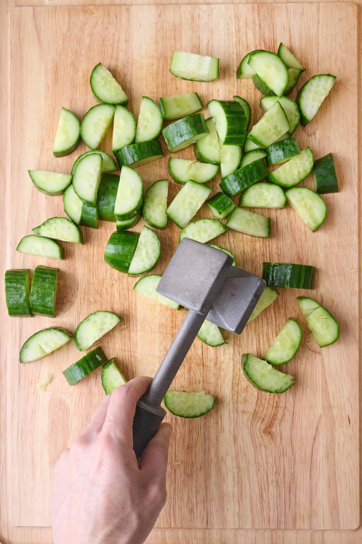 Meat mallet smashing cut cucumbers.