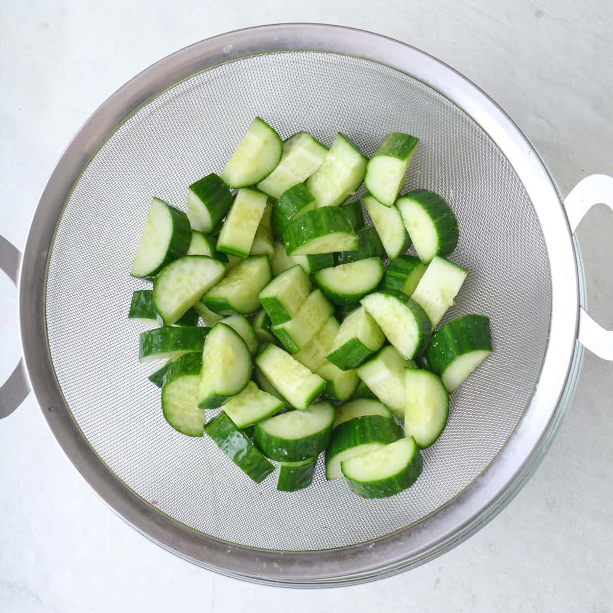 Half moon cucumber slices in a fine mesh sieve.